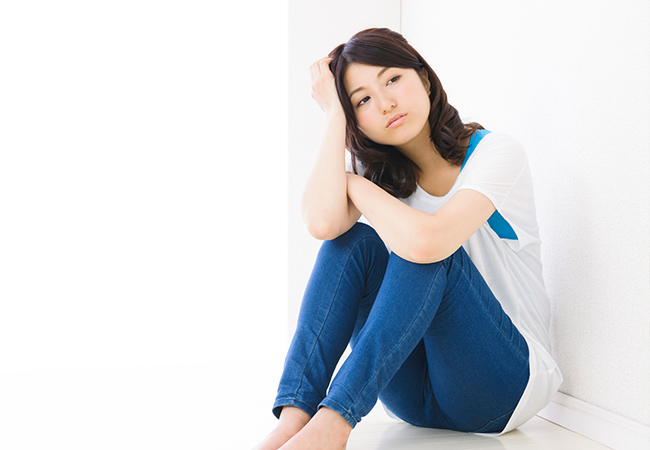 床にすわり考え事をする女性