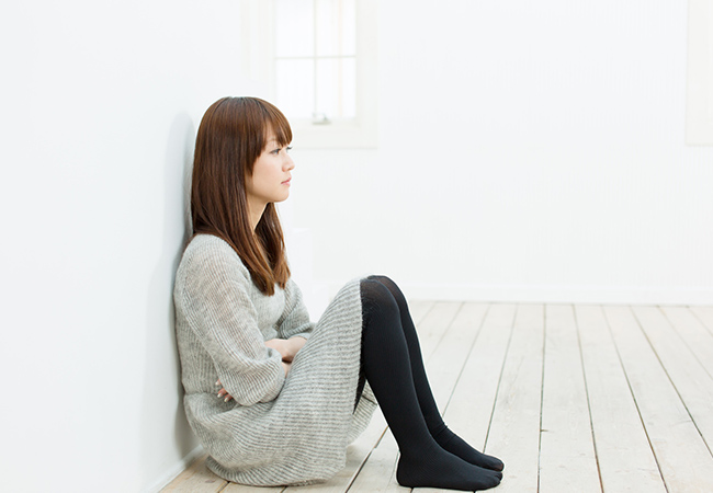 床に座り腕を組み考え事をする女性